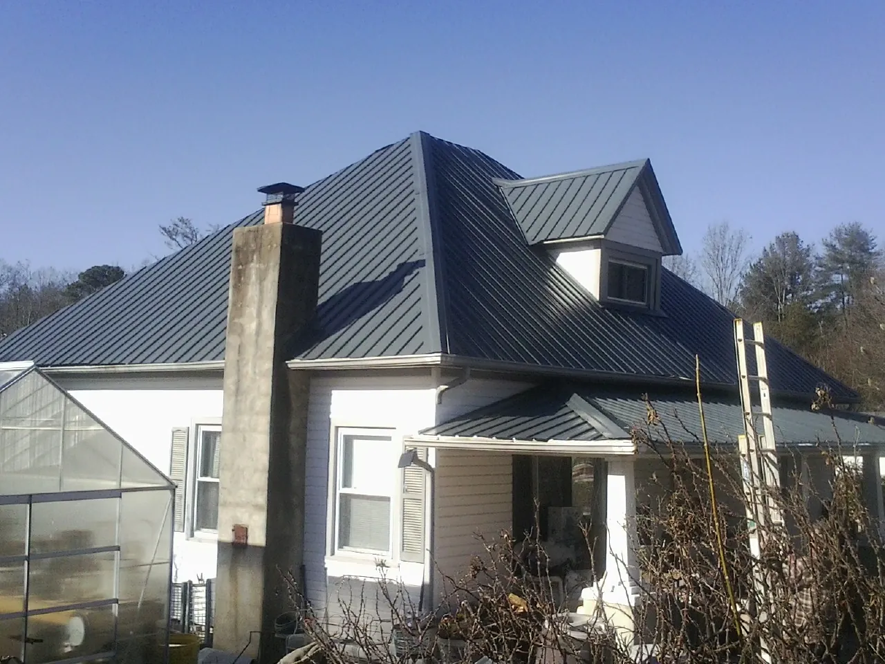 Dark blue standing seam metal roof on a white farmhouse with dormer — Slate & Tile Roof Repair by Roofing Brothers in Kure Beach