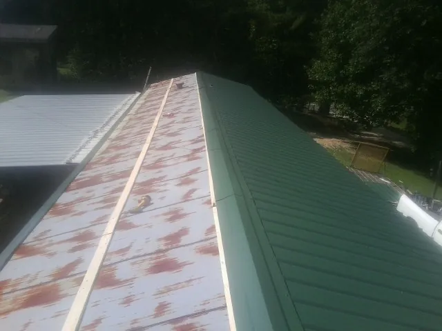 Old rusted panels beside newly installed green metal roofing — Wind Damage Roof Repair by Roofing Brothers in Kure Beach