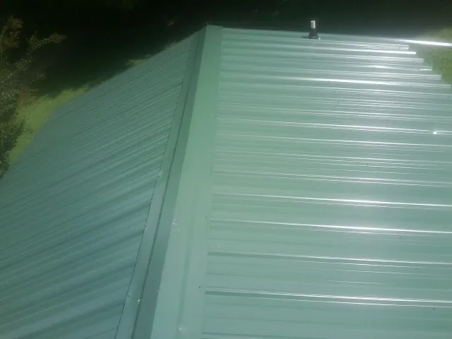 New green metal panels meeting at the ridge of a roof — Flat Roof Repair work by our crew in Kure Beach