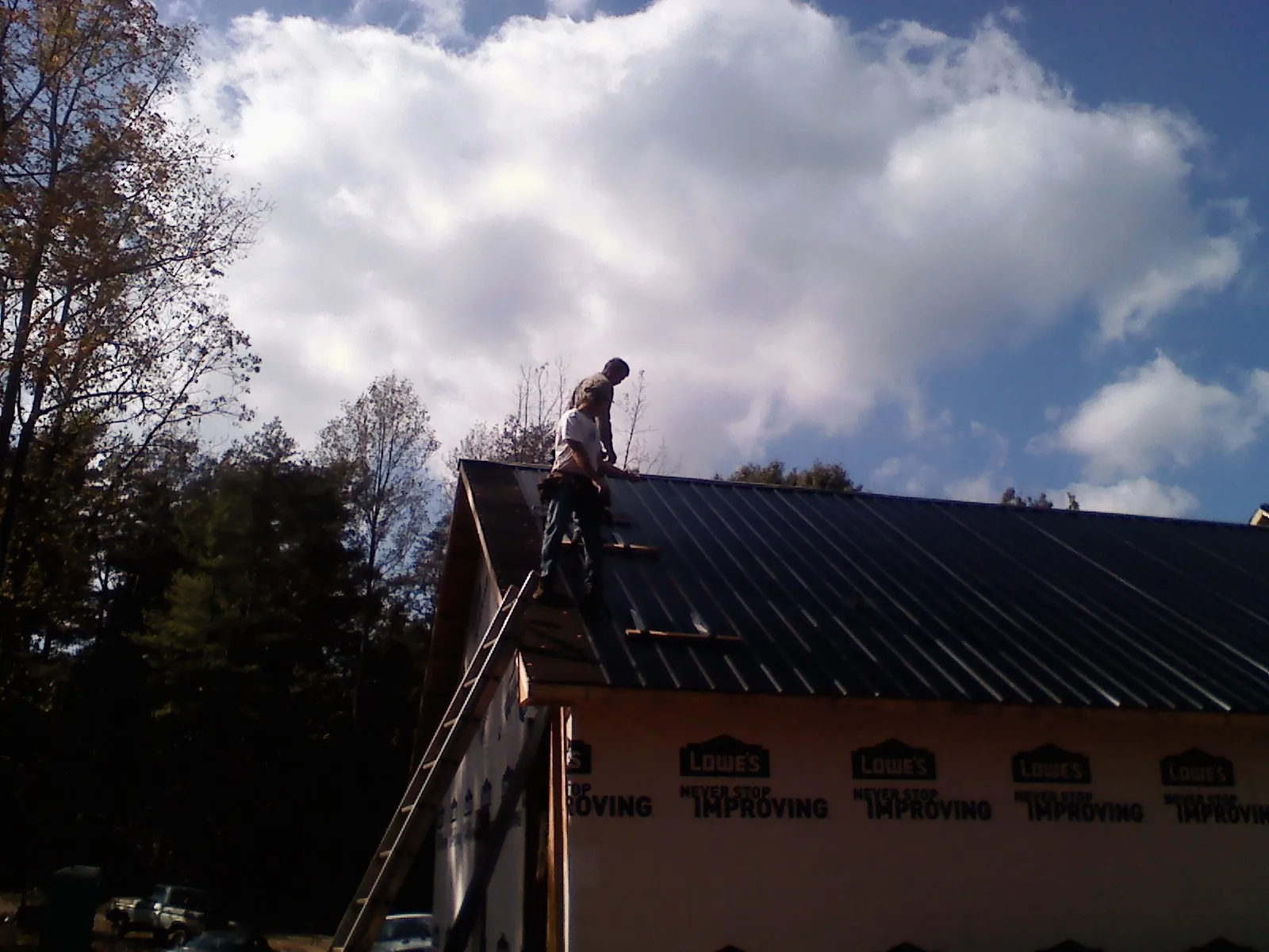 Roofer fastening dark metal panels high against a cloudy sky, from a Roof Inspection job in Kure Beach