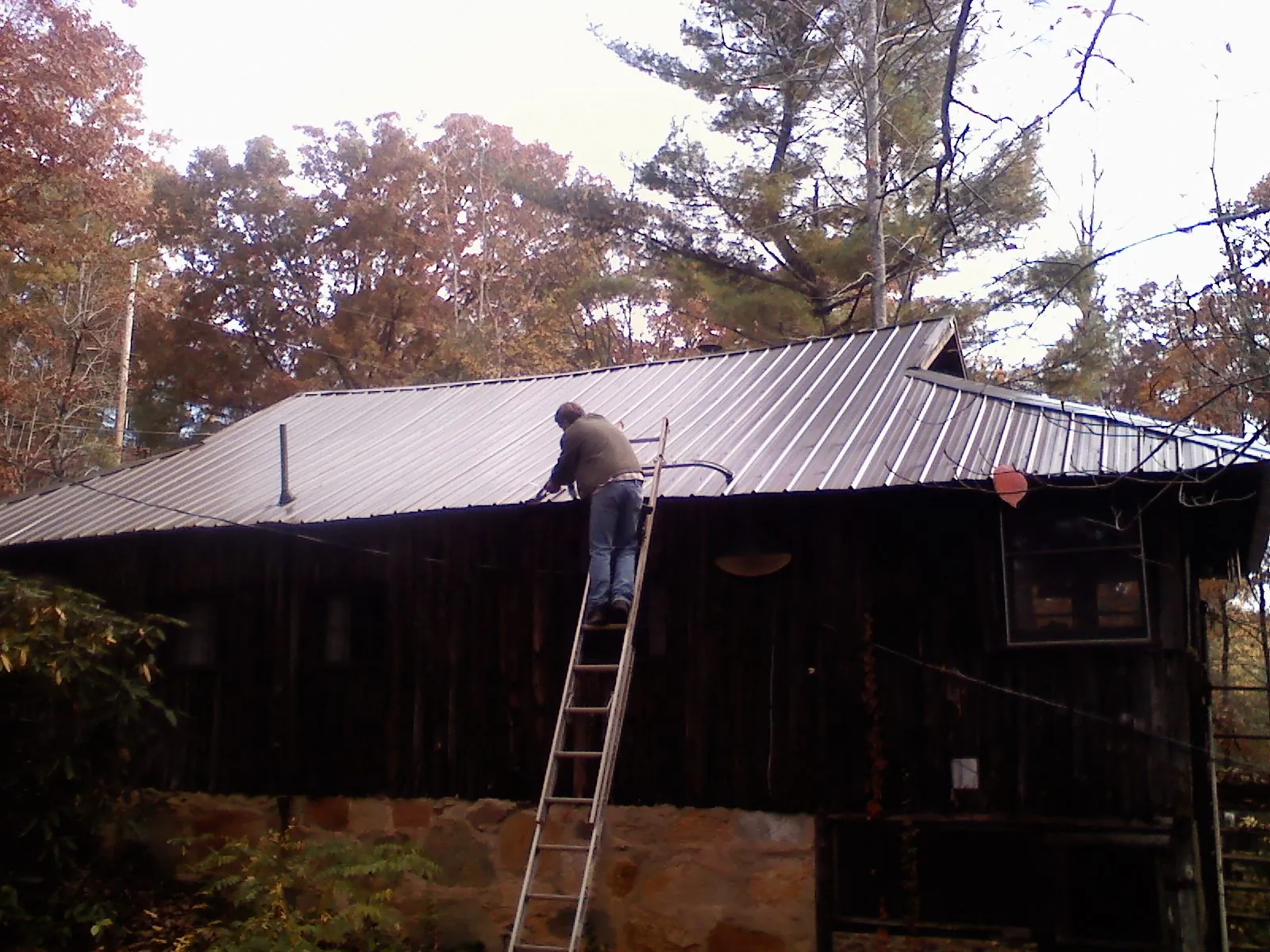 Roofer on a ladder working along the edge of a cabin metal roof in Kure Beach